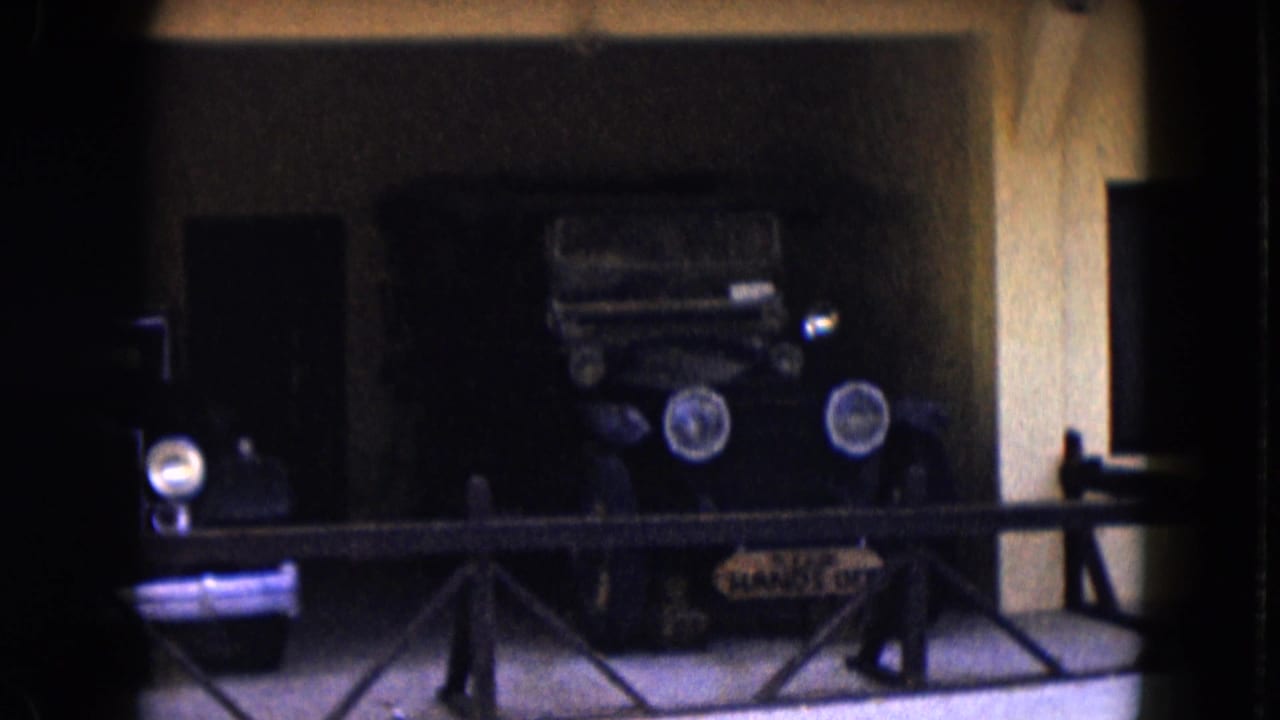 1961 Nevada 8mm frame showing old automobiles on display behind a low railing in a shadowed exhibition space.