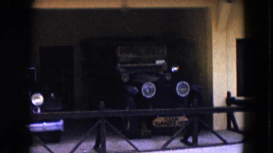 1961 Nevada 8mm frame showing old automobiles on display behind a low railing in a shadowed exhibition space.