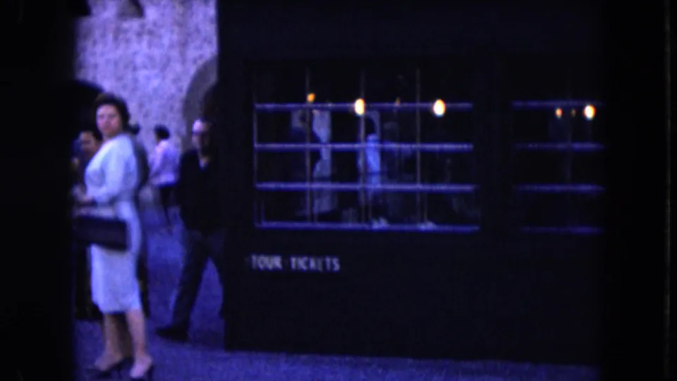 Visitors, including a woman in a light dress, stand near a dark booth marked for tour tickets in the 1961 Nevada footage.