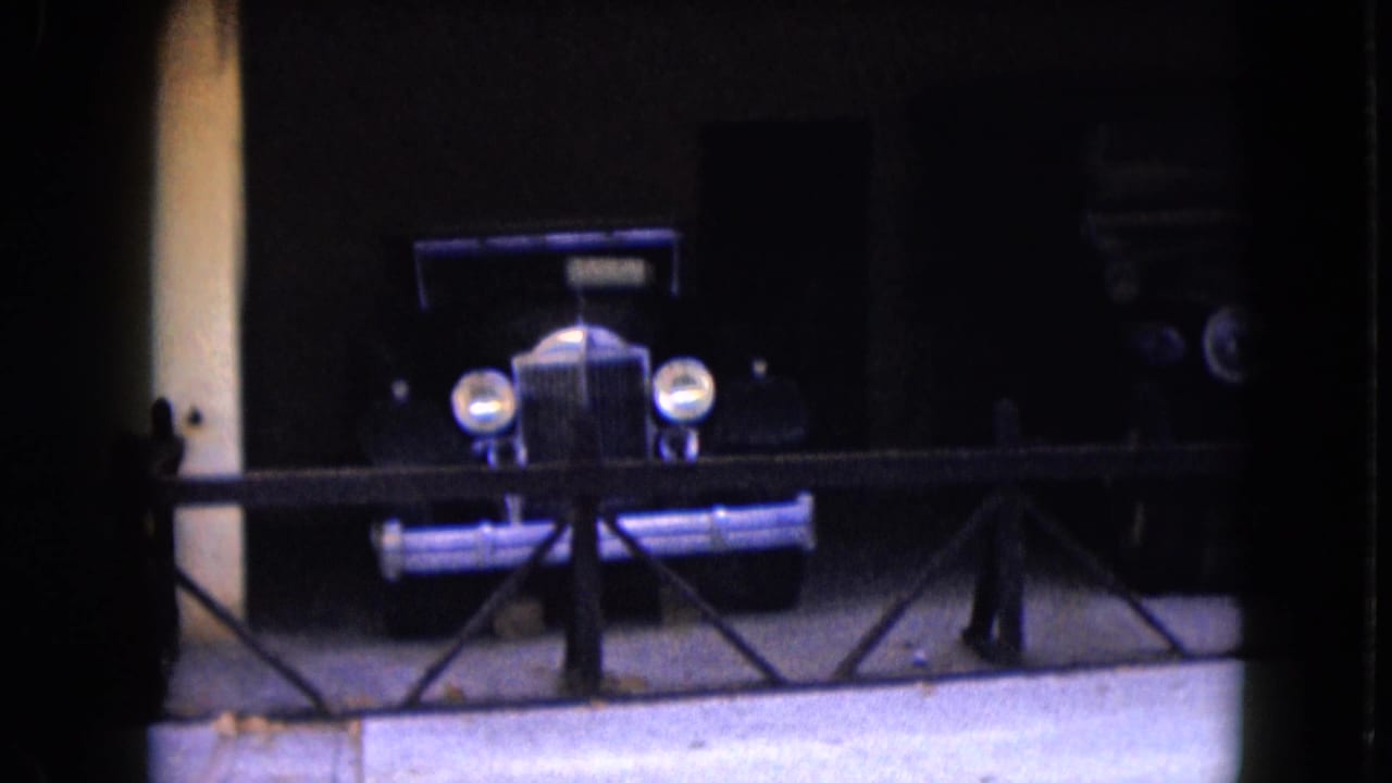 Dark antique car displayed behind a railing in a shaded garage bay.