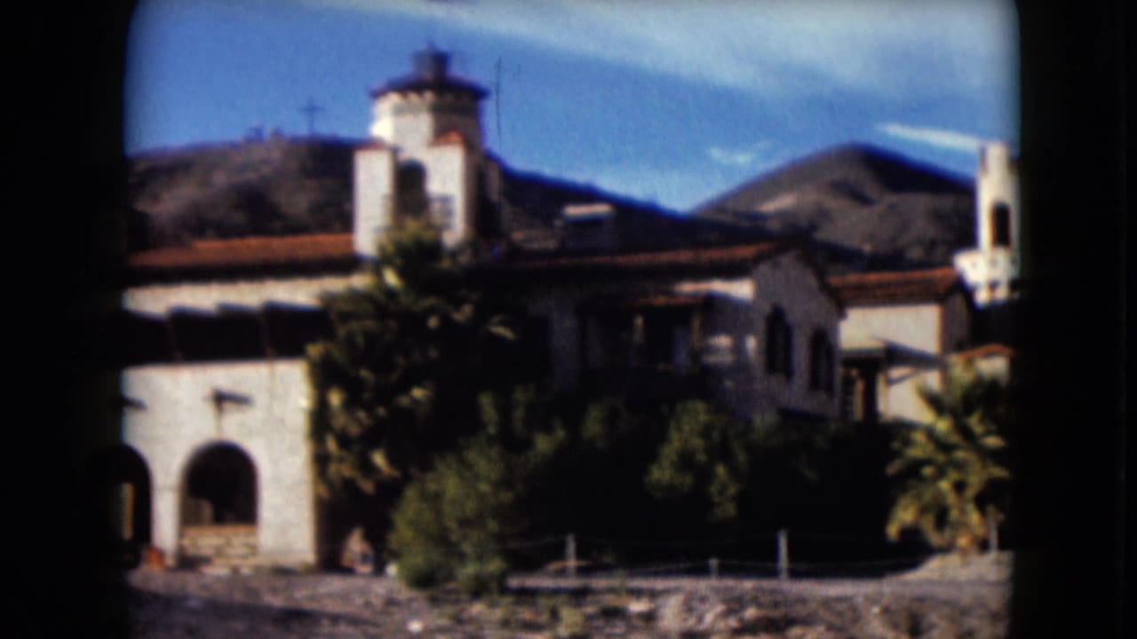 Spanish-style building with arches and tower below desert mountains.