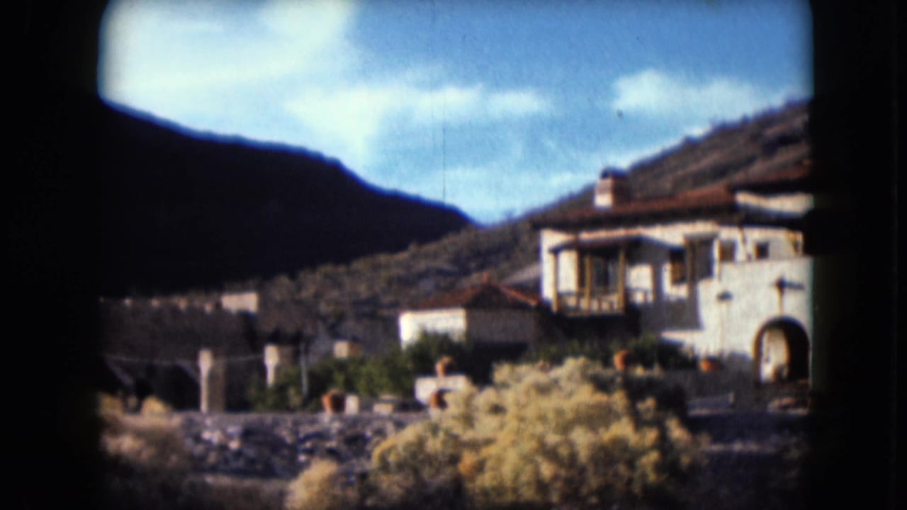 1961 Nevada 8mm frame showing a white Spanish-style building with red tile roof, shrubs, hills, and blue sky.