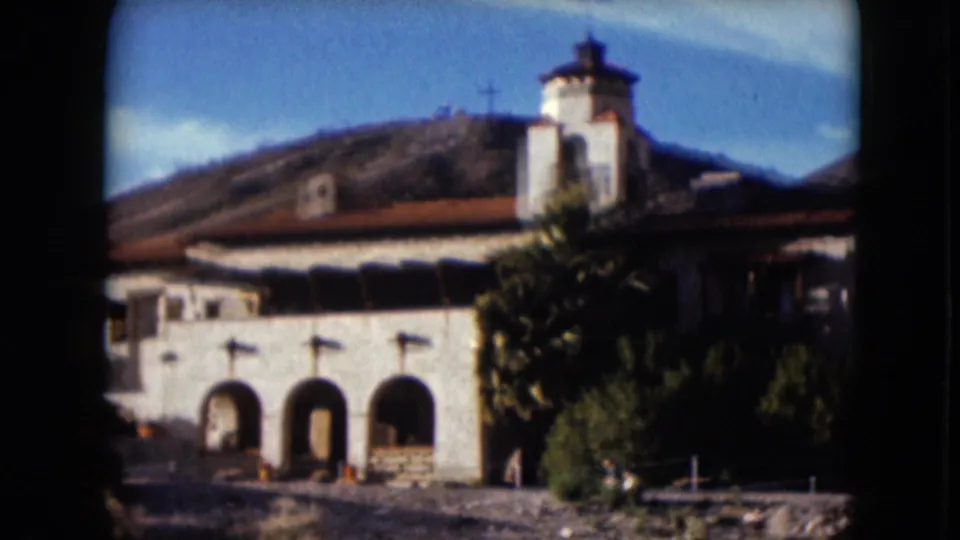 1961 Nevada 8mm frame showing a white stucco facade with three arches, a small tower, red tile roof, and nearby greenery.