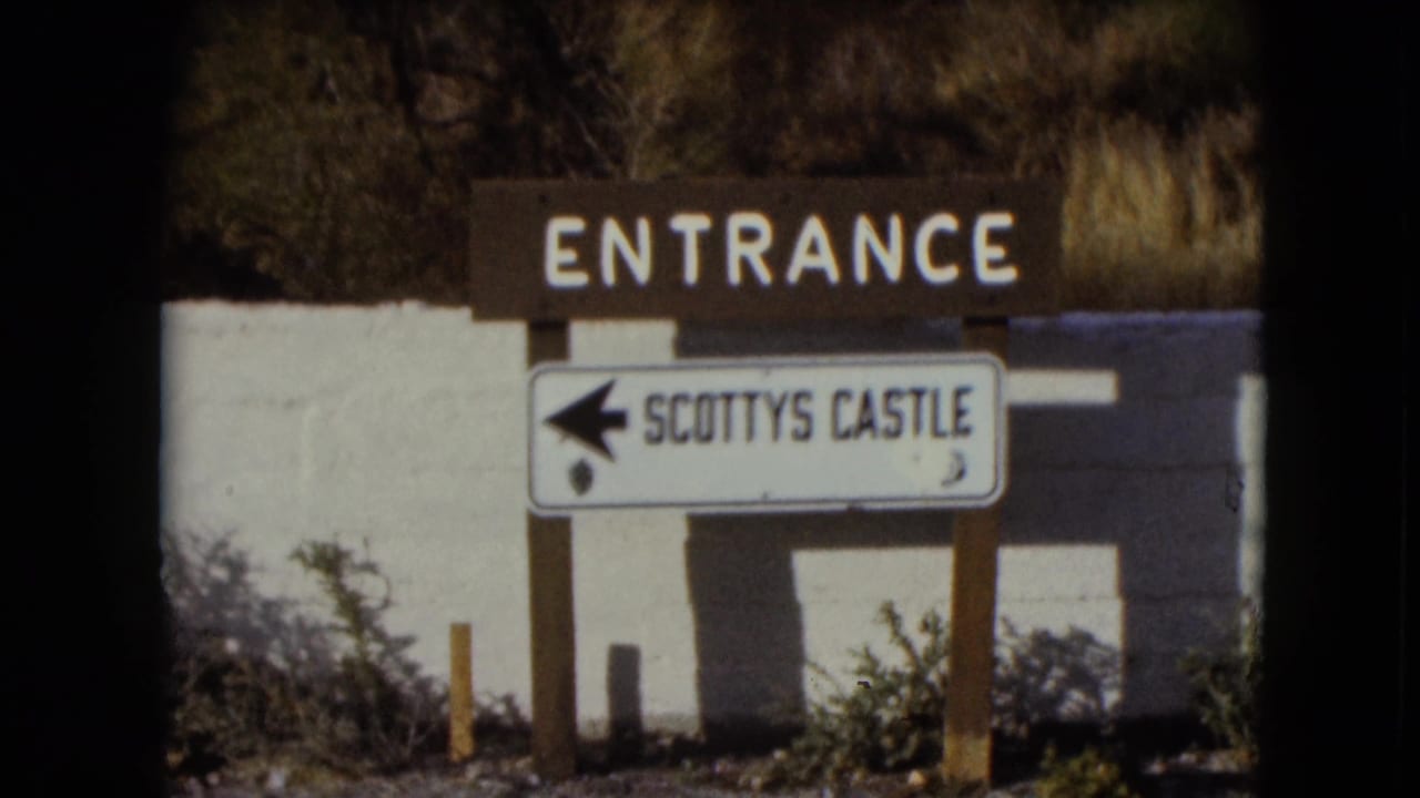 Entrance sign with an arrow pointing to Scotty's Castle beside desert roadside vegetation.