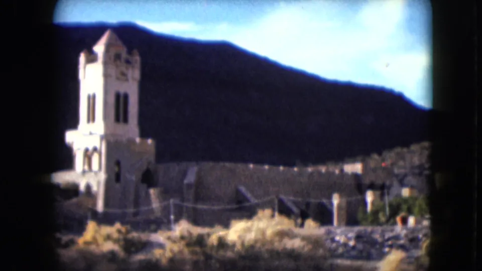 1961 Nevada 8mm frame with Scotty's Castle tower at left, pale walls across the center, and desert vegetation below.