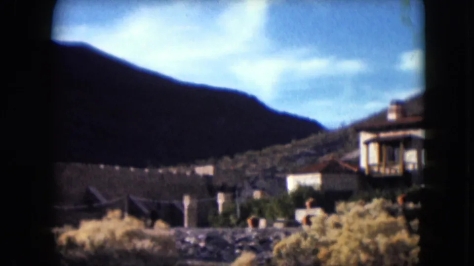 1961 Nevada 8mm frame showing castle walls below a mountain ridge, with a nearby building partly visible at right.