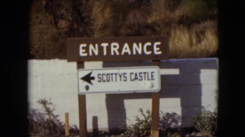 1961 Nevada view of the Scotty's Castle directional sign, with a left arrow beneath the ENTRANCE board and dry vegetation behind it.