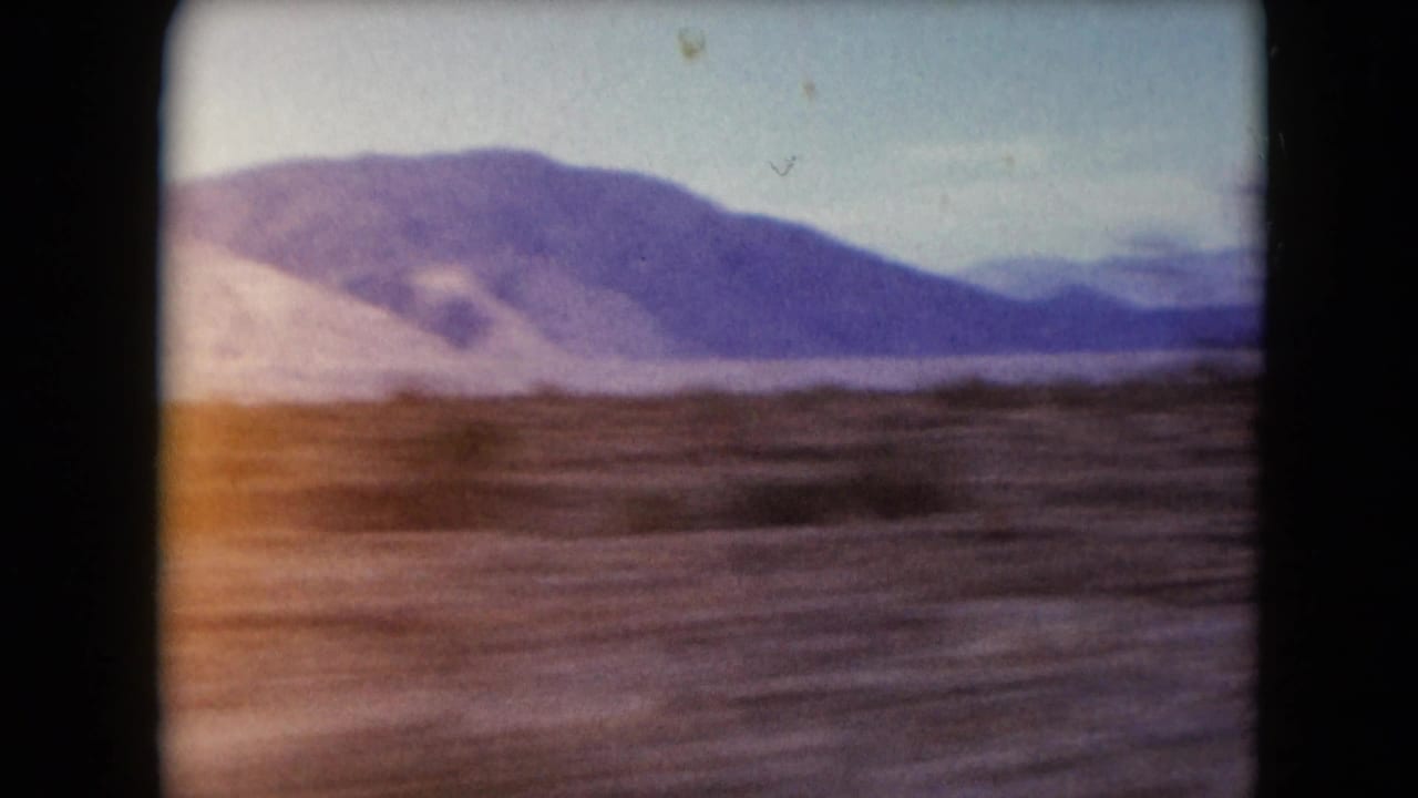 Open desert plain and low mountains viewed from a moving roadside perspective.