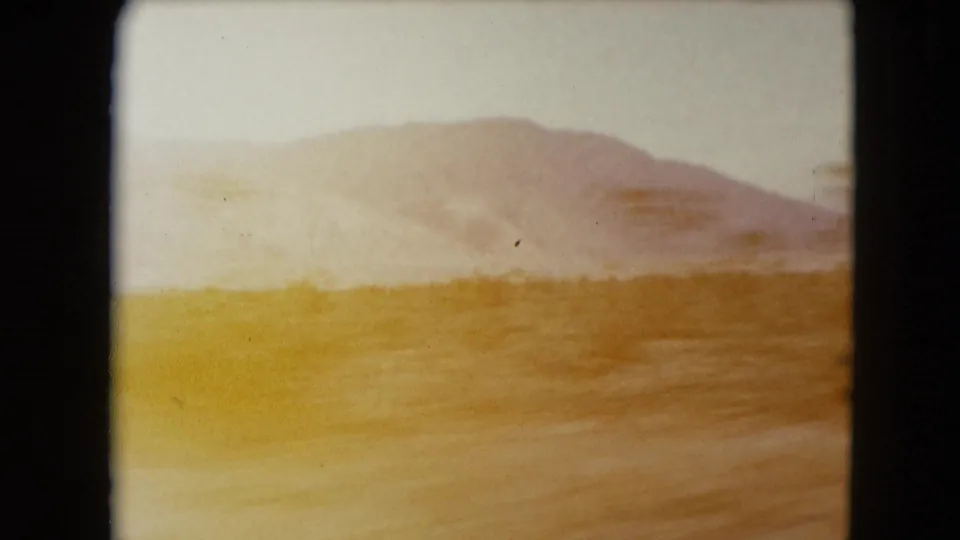 Warm exposed 8mm frame of Nevada desert terrain, low hills and roadside blur during the drive.