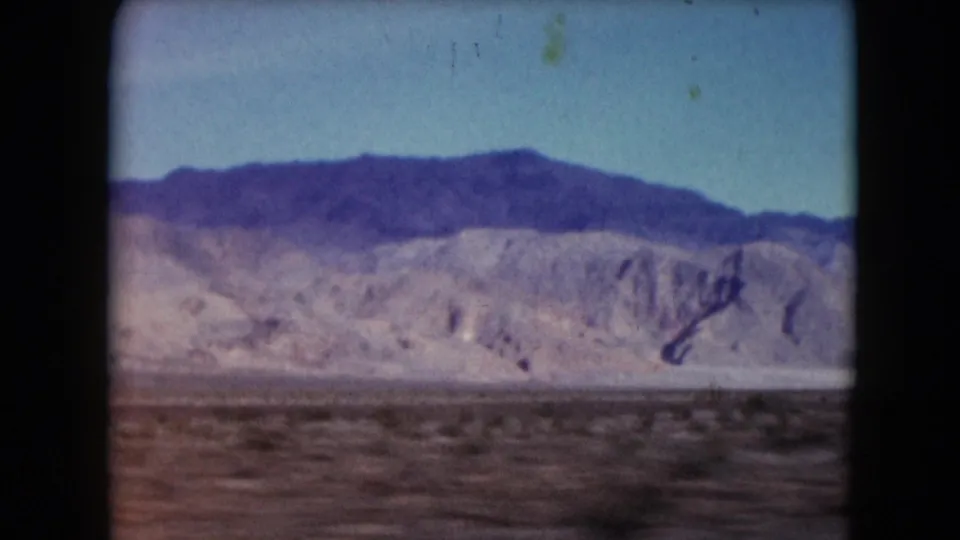 1961 Nevada 8mm frame showing closer arid hills, a dark ridge line, sparse foreground brush, and faded blue-purple color.