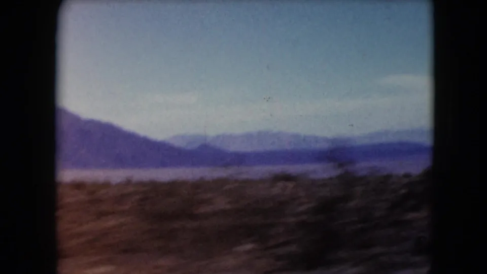 1961 Nevada home-movie frame with motion-blurred desert foreground, layered distant mountains, and open blue sky.
