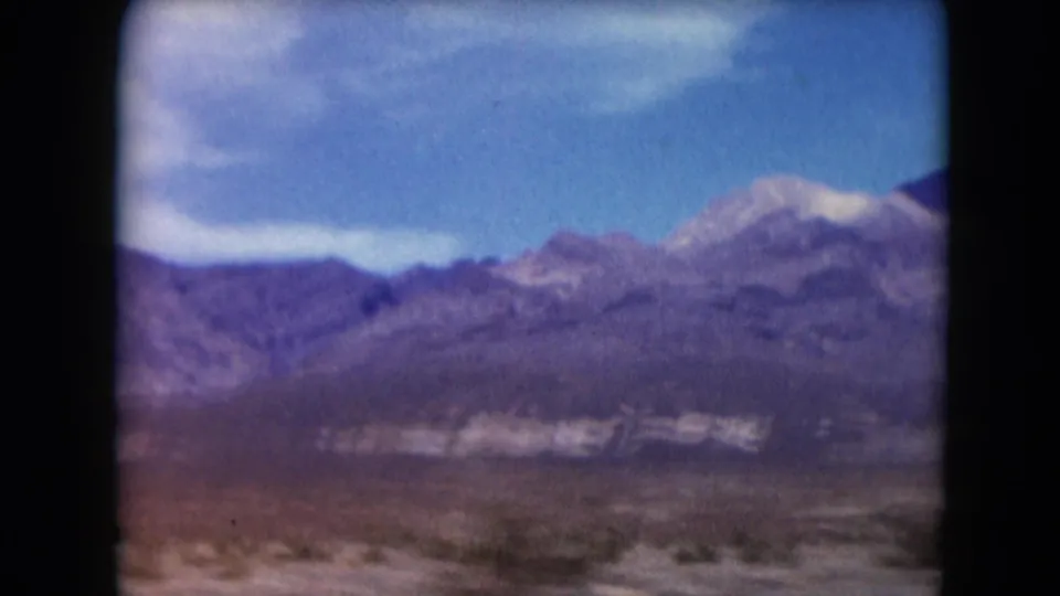 1961 Nevada 8mm frame showing a dry plain and layered mountain ridges seen from a moving car.