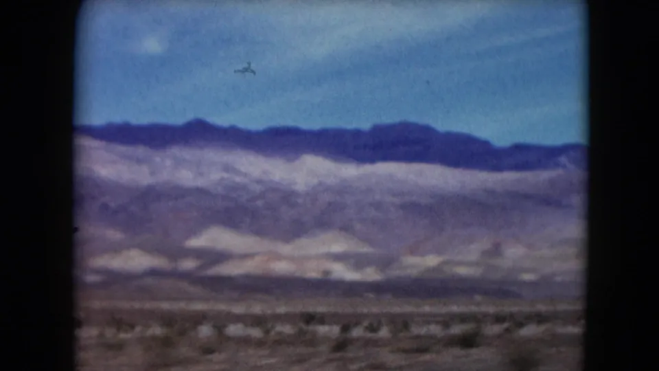 1961 Nevada home-movie frame with a long mountain horizon, dry plain, sparse scrub, and visible 8mm grain.