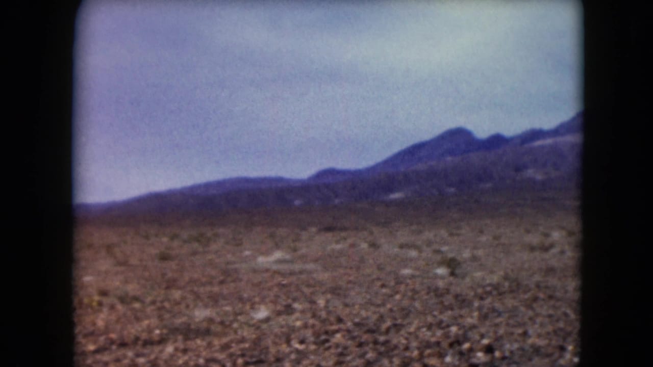 Rocky desert foreground with brush and a dark mountain ridge in the distance.