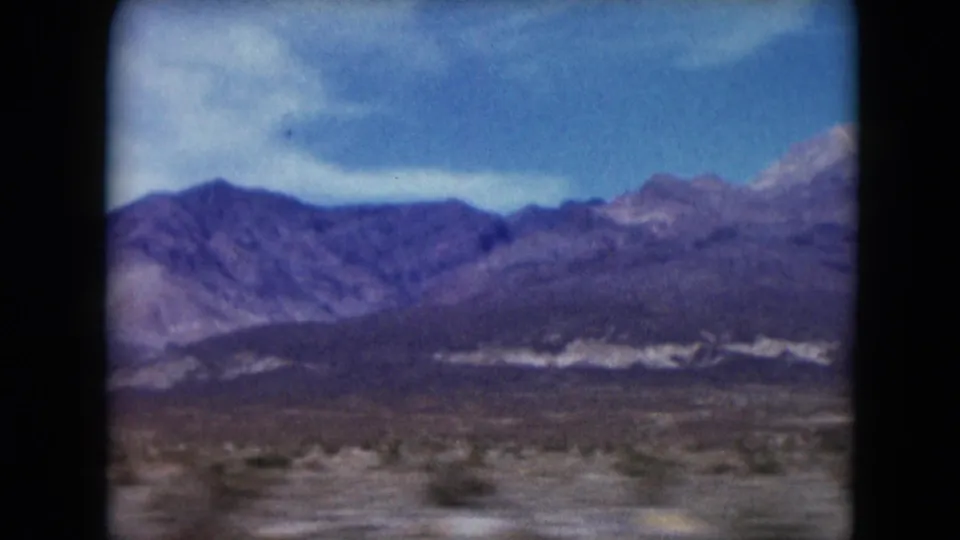 1961 Nevada home-movie frame with rugged mountain slopes, desert brush, and open foreground seen through soft 8mm color.