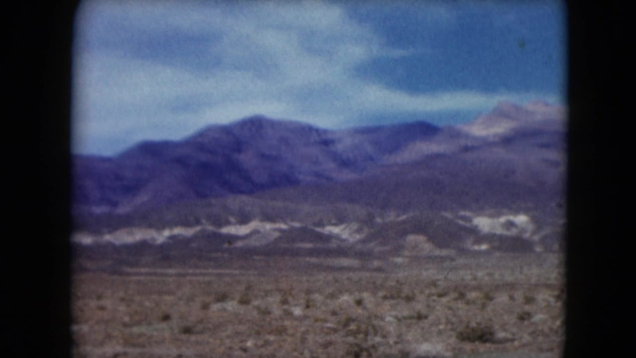 1961 Nevada desert view with scrubby foreground, low pale ridges, and darker mountain range across the horizon.