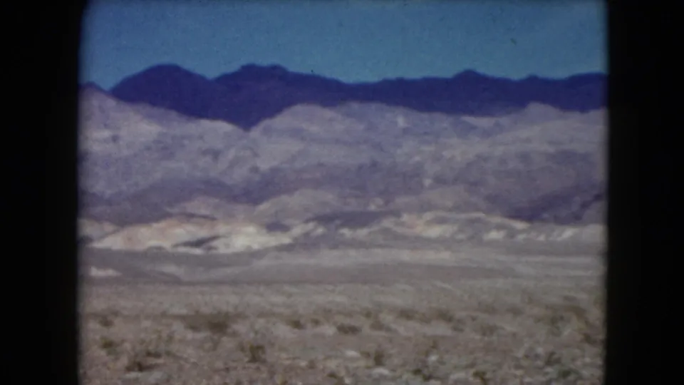 1961 Nevada home-movie still with scrubby desert foreground, pale foothills, and darker mountain ridges in the distance.