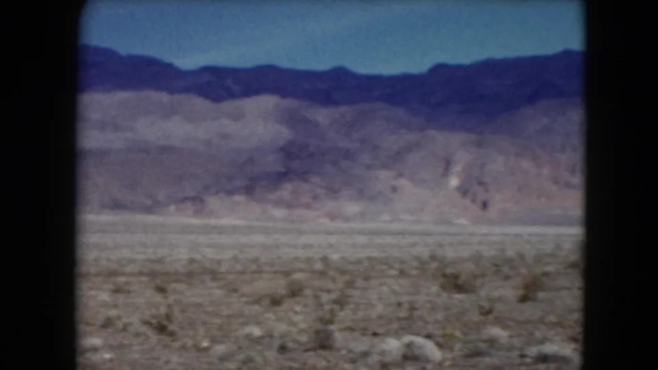 Soft 8mm frame from 1961 Nevada showing rocky scrub foreground and distant layered mountains across an open desert basin.