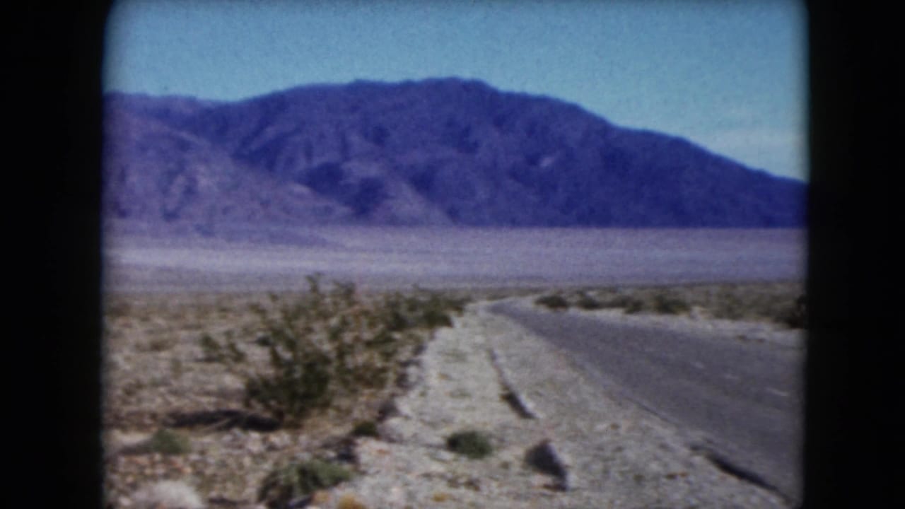 1961 Nevada 8mm frame showing a paved road curving through arid desert scrub toward distant mountains.