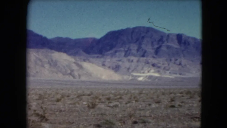 Faded 8mm view of a Nevada desert valley in 1961, with low vegetation and a mountain range across the horizon.