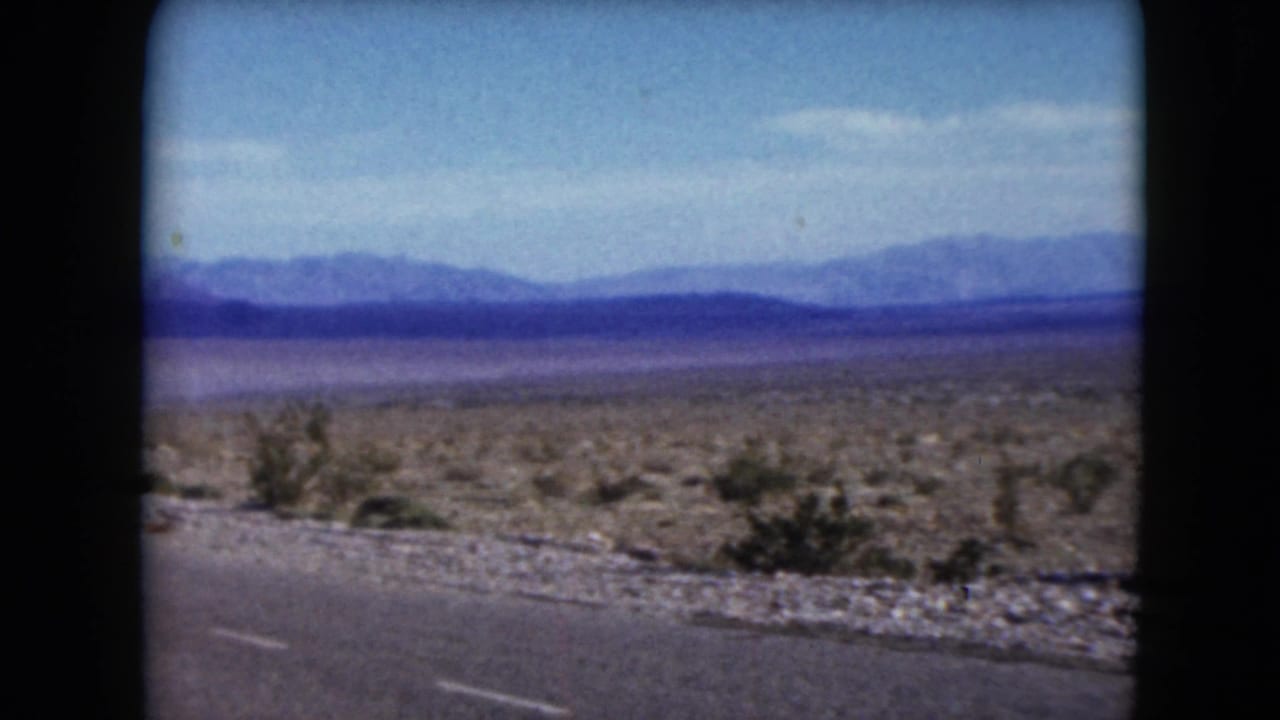 Open desert plain beside a paved road with low brush and distant mountain ridges.