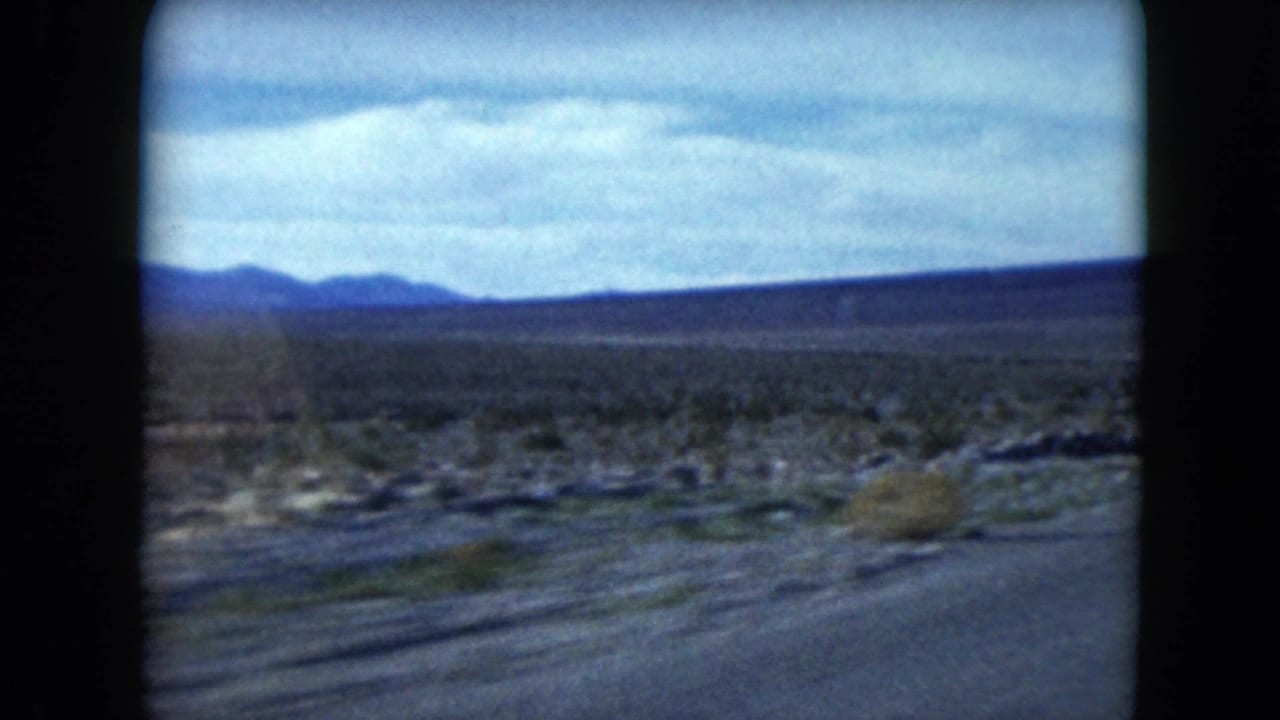 Moving 8mm road-trip view across Nevada desert terrain toward low blue mountain ridges.