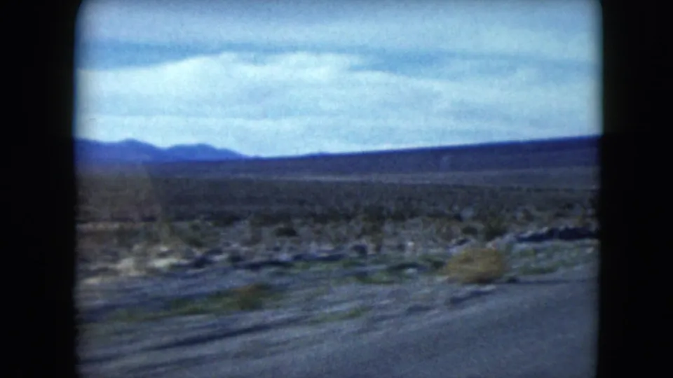 Moving 8mm road-trip view across Nevada desert terrain toward low blue mountain ridges.