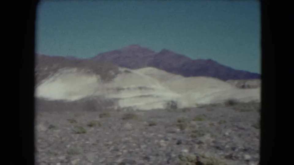 1961 Nevada 8mm view of light desert mounds, scattered shrubs, and a distant mountain ridge.