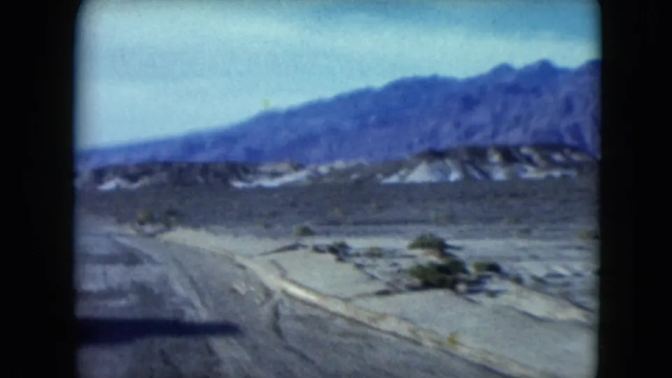 1961 Nevada home-movie frame showing a curving desert road, scrubby ground, mountain foothills, and faded 8mm color.