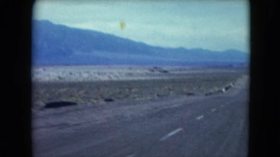 1961 Nevada road-travel frame showing a curving highway through desert flats with mountains across the horizon.