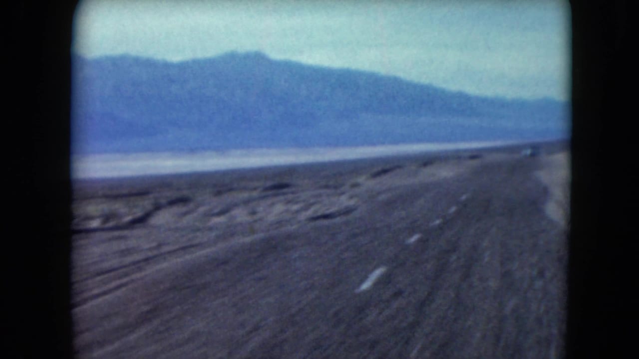 Forward view down a paved desert highway with mountains in the distance.
