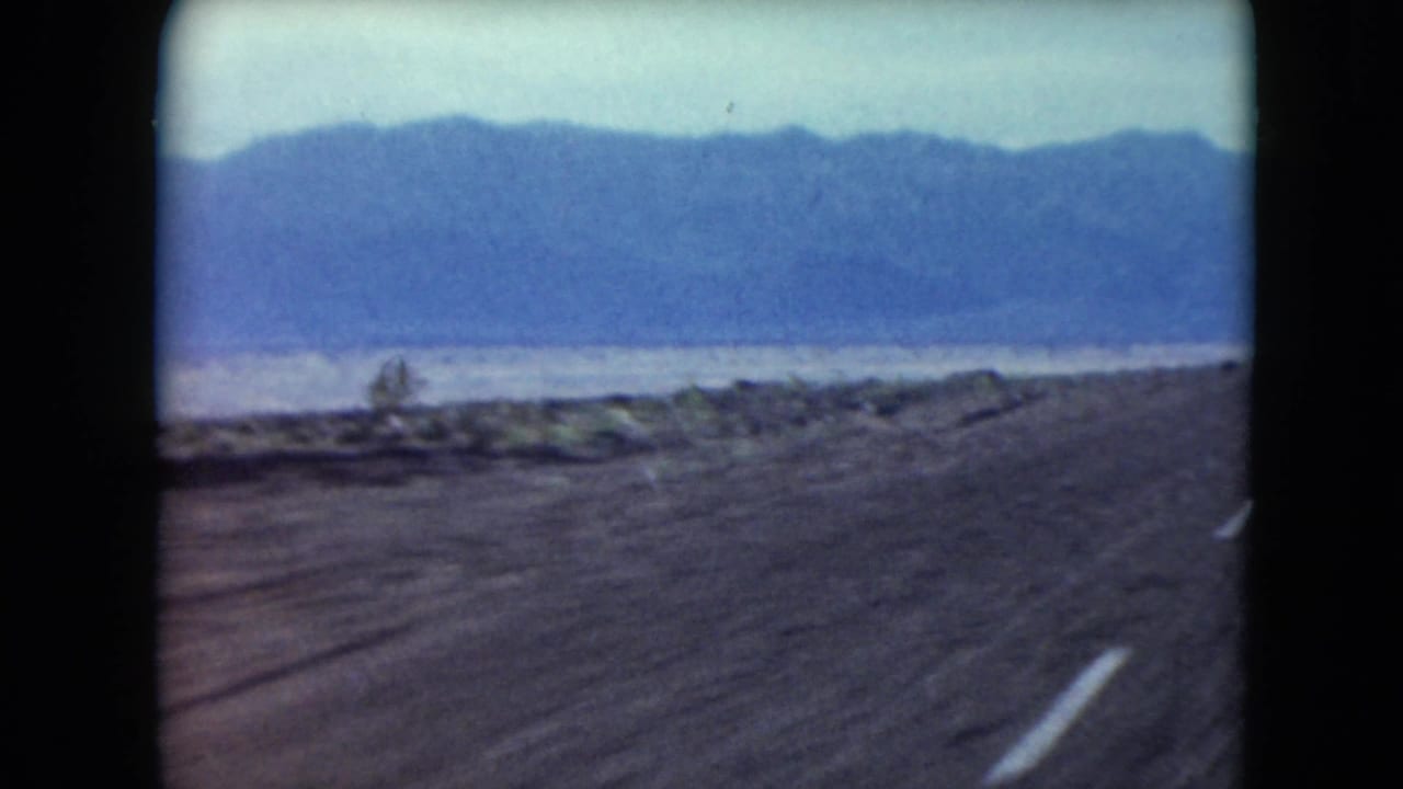 1961 Nevada 8mm view down a blacktop desert road toward distant blue mountains under a pale sky.