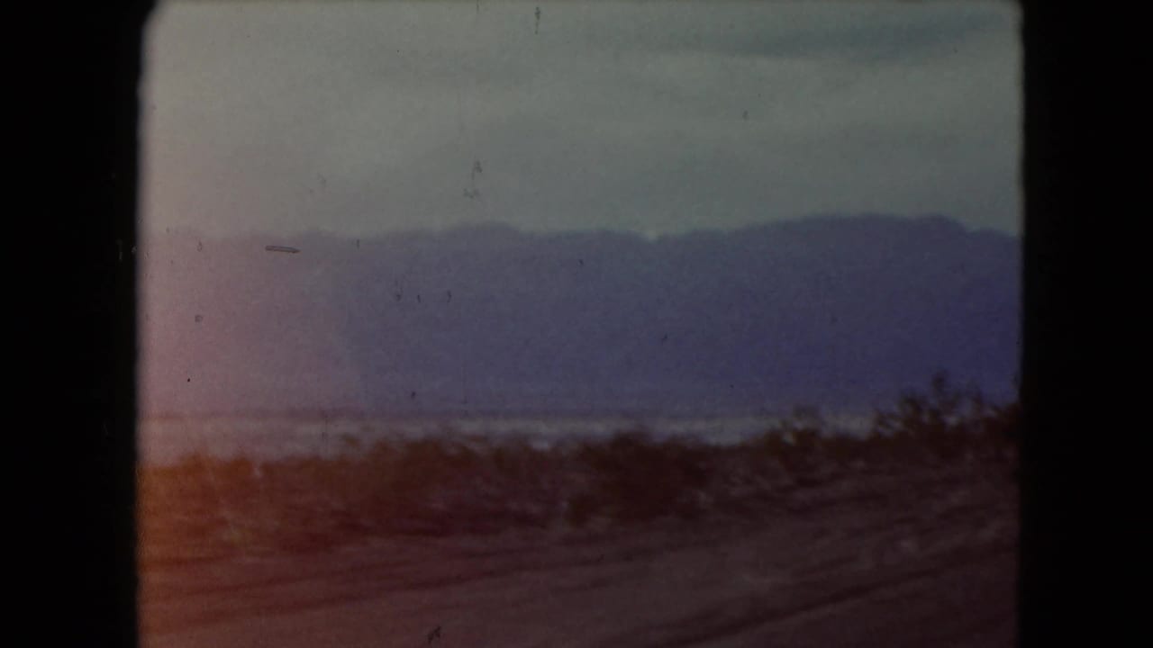 1961 Nevada desert travel view with purple-blue mountains, sparse brush, and a dusty roadside foreground.