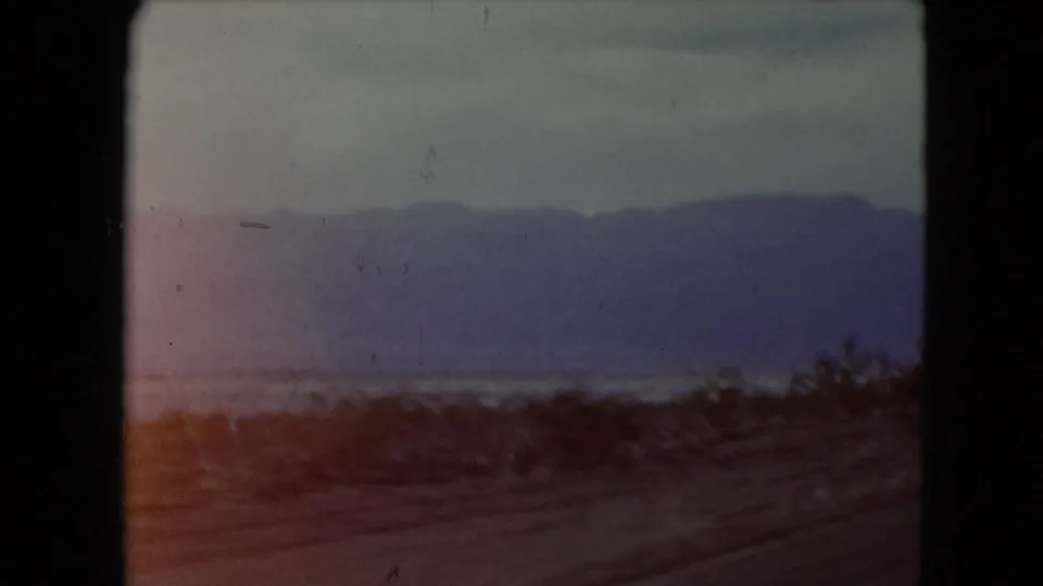 1961 Nevada desert travel view with purple-blue mountains, sparse brush, and a dusty roadside foreground.