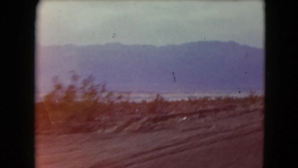 Nevada home-movie frame from 1961 showing motion-blurred brush, a dirt road foreground, and mountains in the distance.