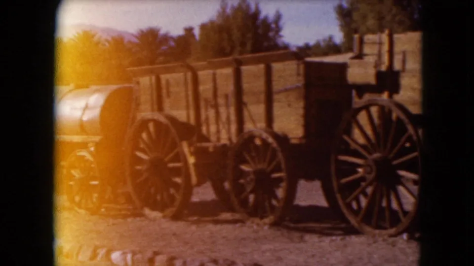 1961 Nevada 8mm frame showing a cylindrical water tank wagon near a wooden wagon with large spoked wheels.