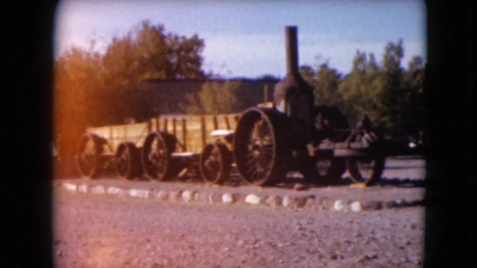 1961 Nevada frame showing the side of an antique steam traction engine beside low stones, trees, and hills.