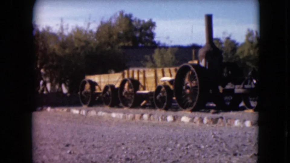 Faded 8mm frame of an antique steam traction engine display in Nevada, with gravel foreground, trees, and distant hills.