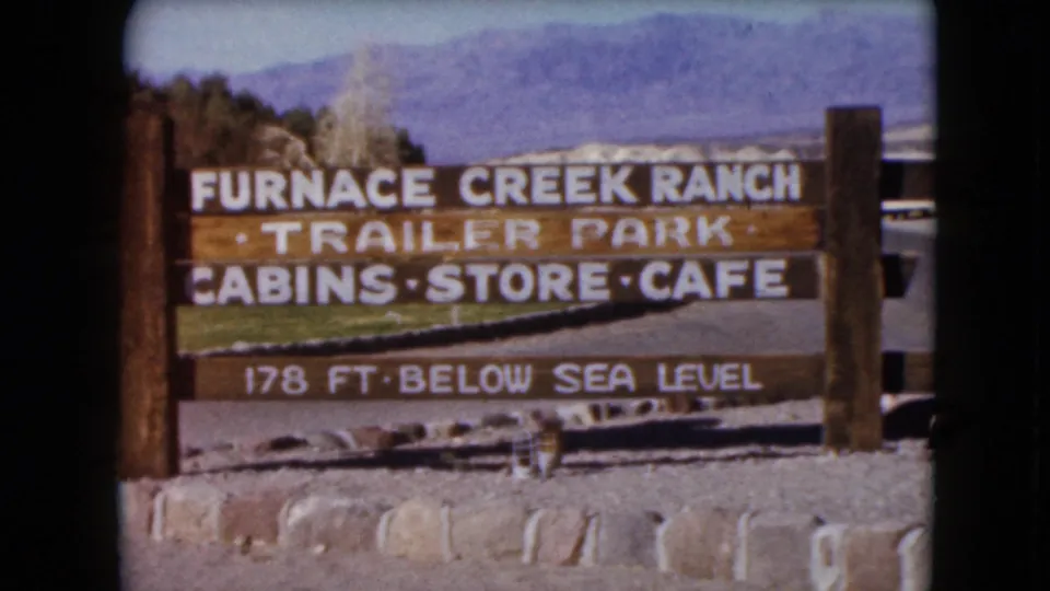 1961 8mm frame holding on the Furnace Creek Ranch sign with trailer park and cabin-store-cafe wording against distant mountains.