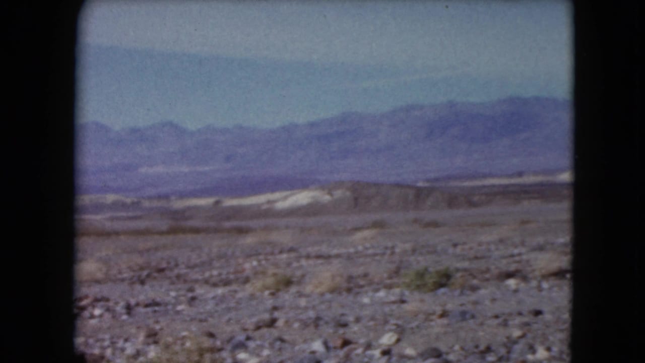 1961 Nevada desert view with pale flats, low ridges, and a distant mountain range seen through an 8mm frame.