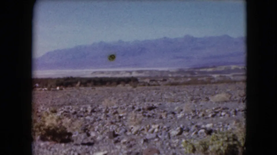 1961 Nevada frame with a wide arid foreground, scattered shrubs, a pale salt-flat-like horizon, distant mountains, and 8mm scan borders.