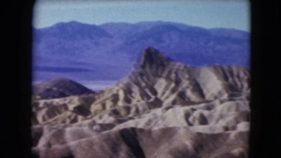 1961 Nevada 8mm frame with a jagged tan rock formation rising before layered blue-purple mountain ranges.