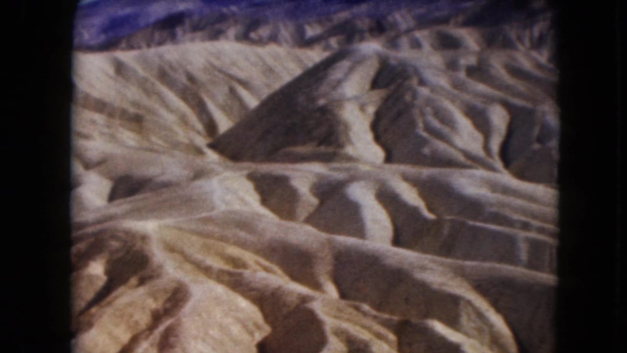 1961 Nevada 8mm frame showing pale desert badlands with rounded ridges, deep erosion channels, and dark gate borders.