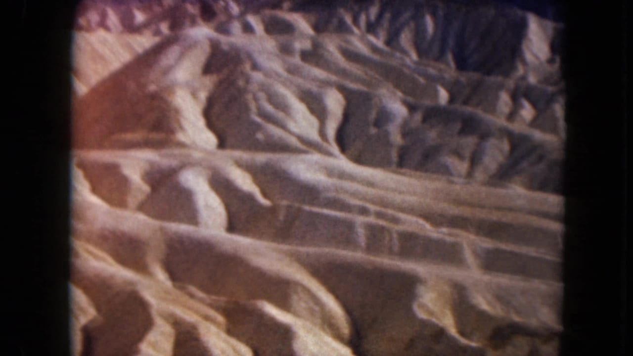 1961 Nevada home-movie frame of sunlit desert badlands, with rounded sandstone-like forms and visible black film-frame borders.