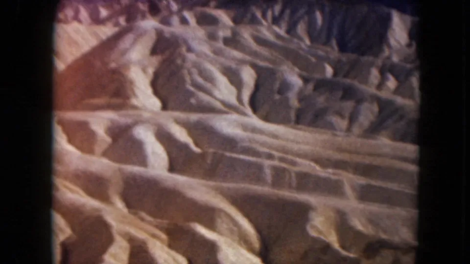1961 Nevada home-movie frame of sunlit desert badlands, with rounded sandstone-like forms and visible black film-frame borders.