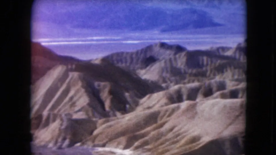 1961 Nevada 8mm travel view with eroded foreground hills, distant mountain ridges, and a blue sky across the horizon.
