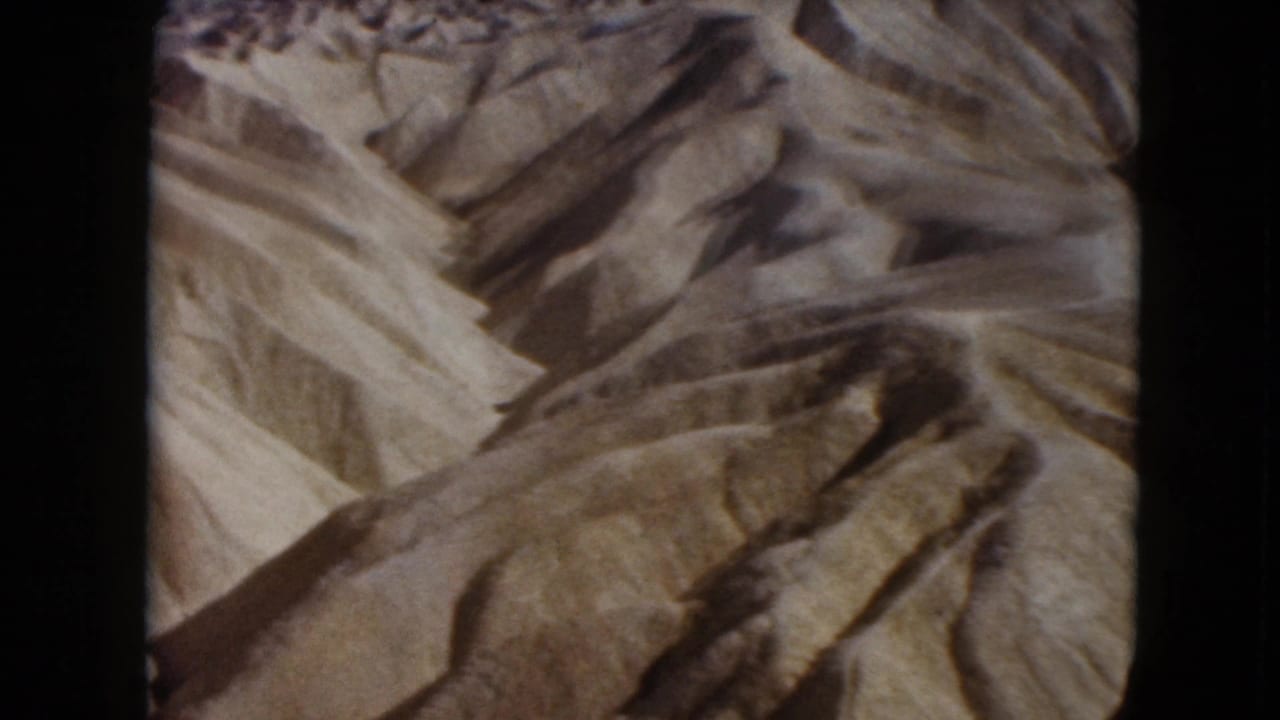 1961 Nevada 8mm frame showing barren tan desert slopes carved by erosion, with no people, roads, or plants visible.