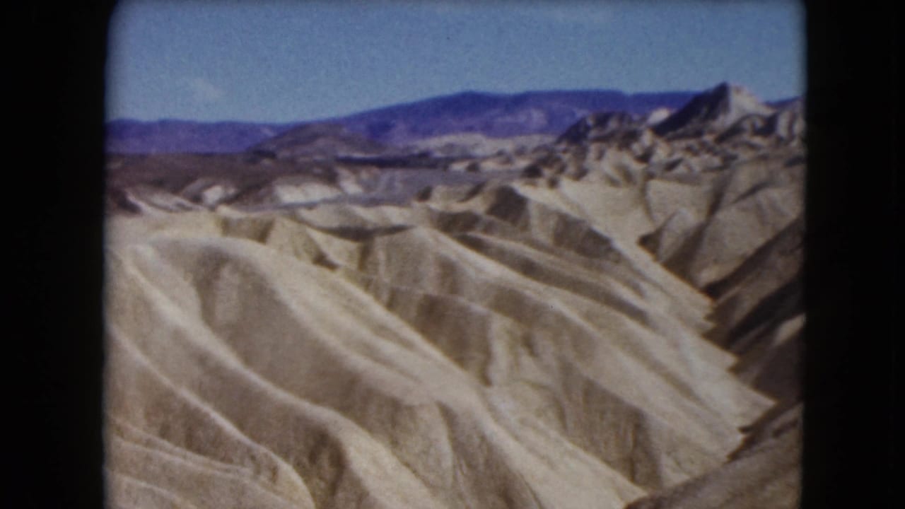 1961 Nevada 8mm view across barren eroded hills toward darker mountain ranges beneath a clear blue sky.