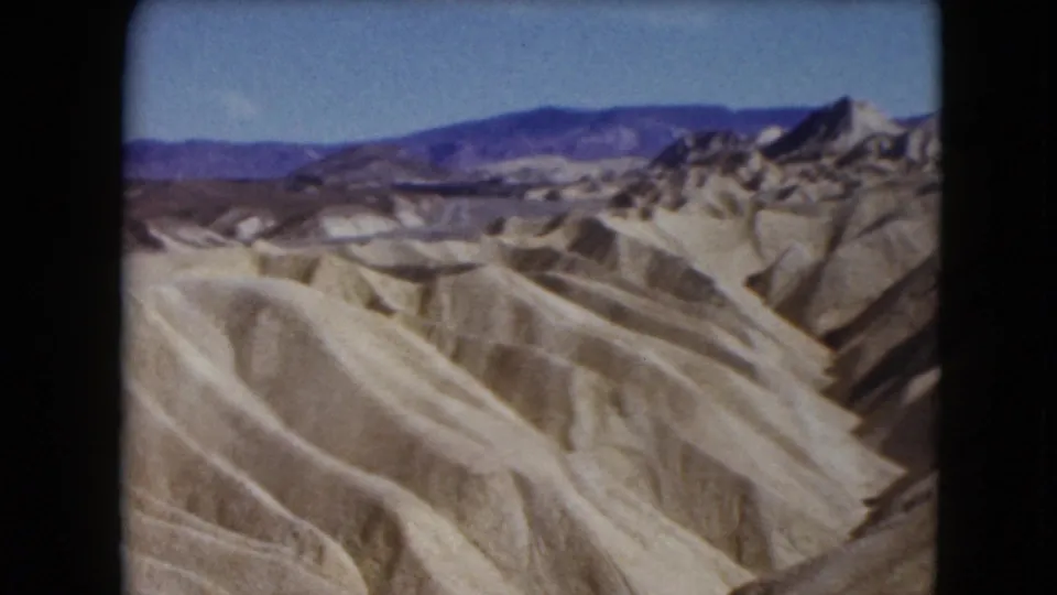 1961 Nevada 8mm view across barren eroded hills toward darker mountain ranges beneath a clear blue sky.