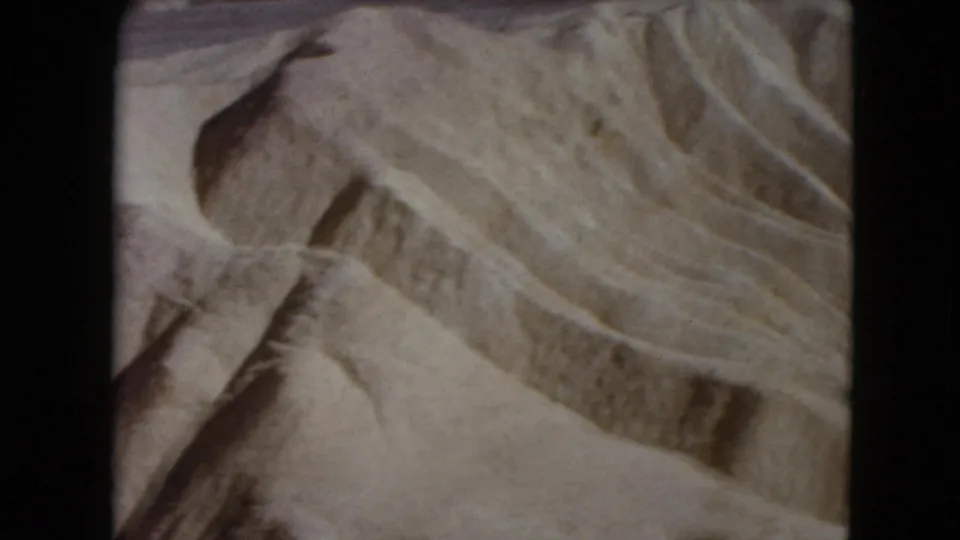 1961 Nevada desert frame with diagonal dune ridges, muted tan sand, and shadowed natural patterns in an 8mm scan.
